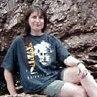 A person wearing a printed shirt and shorts sitting on rocks.