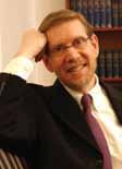A man in a suit smiling, with bookshelves in the background.