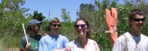 Four people smiling outdoors with trees in the background. 