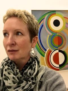 A person with a patterned scarf in front of colorful wall art.
