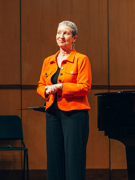 Teresa McCollough standing on stage wearing an orange jacket.