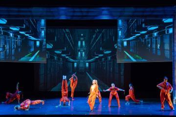 Stage performance of Legally Blonde with actors in pink-orange outfits against a blue backdrop.