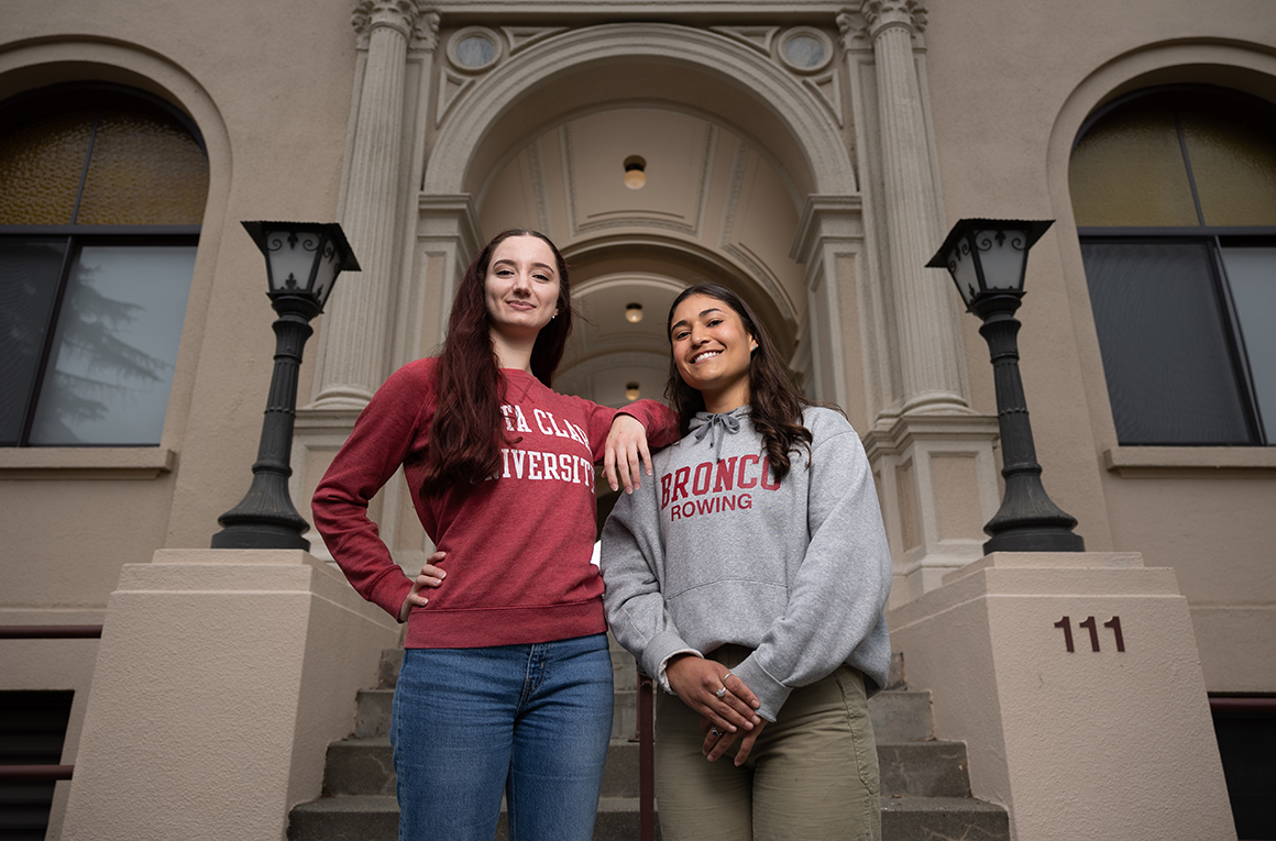 Two students stand at the foot of a staircase by a buildings arched entrance. image link to story