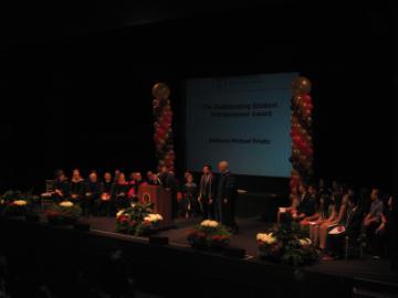 Large group on stage with lighting and a central screen displaying 2012 OSE.