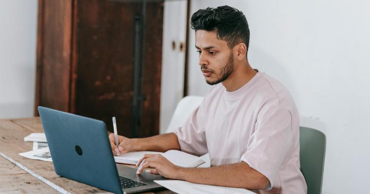 Student working on laptop while taking notes by hand image link to article