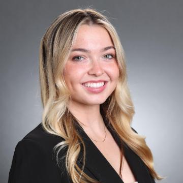 A woman with a smile dressed in business attire against a gray background 