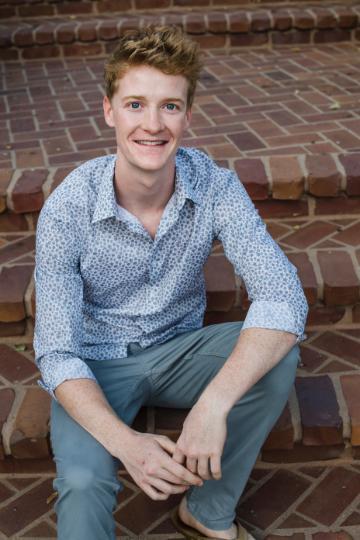 A person sitting on brick steps, smiling, titled Cole Normandin.