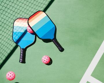 Two pickleball paddles and three balls on a pickleball court.