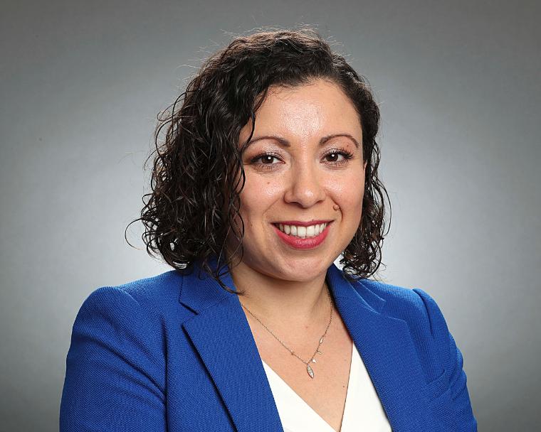 A person in a blue blazer smiling against a grey background.