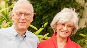 An elderly man and woman are smiling in an outdoor setting.