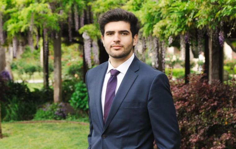A man in a blue suit and purple tie standing in the mission gardens