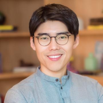 A person smiling, wearing glasses and a blue shirt.