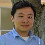 A person in a blue shirt standing in front of a tree.