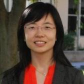 A woman smiling, wearing glasses, with a blurred background.