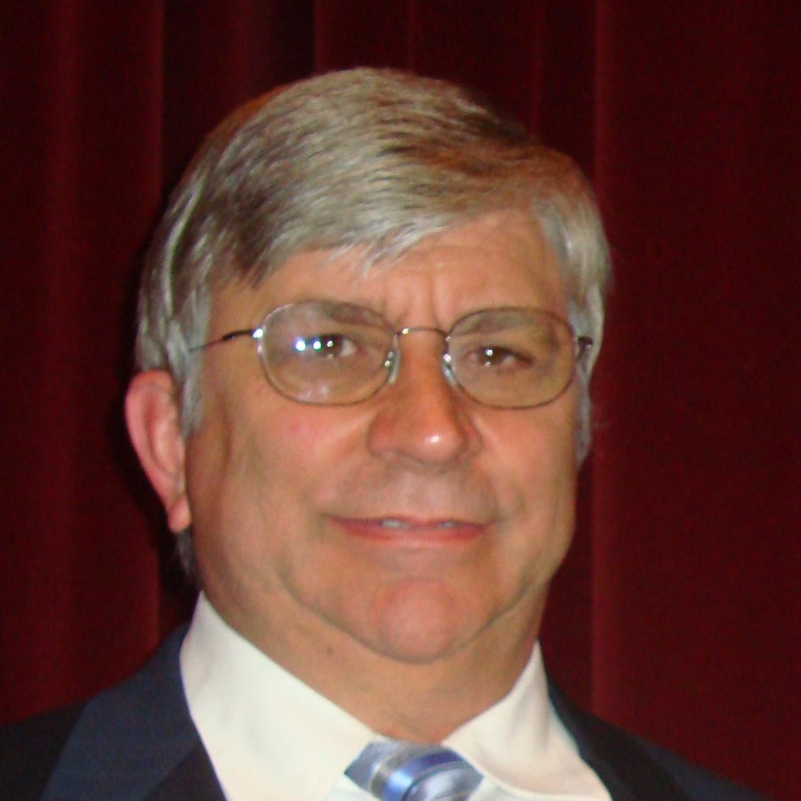 A man smiling in front of a red background.