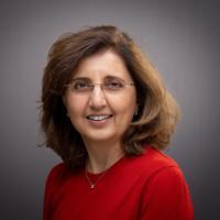 A woman in a red shirt smiles against a grey background. image link to story